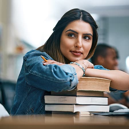 Student rests chin on hands folded over stack of books