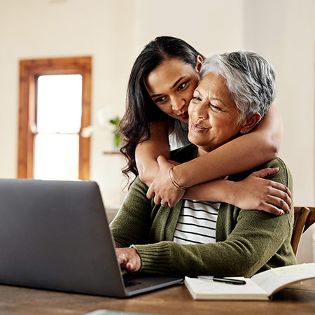 Adult daughter hugs mother as they both look at laptop