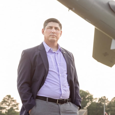 Jason Delucy dressed business casual standing under a military plane