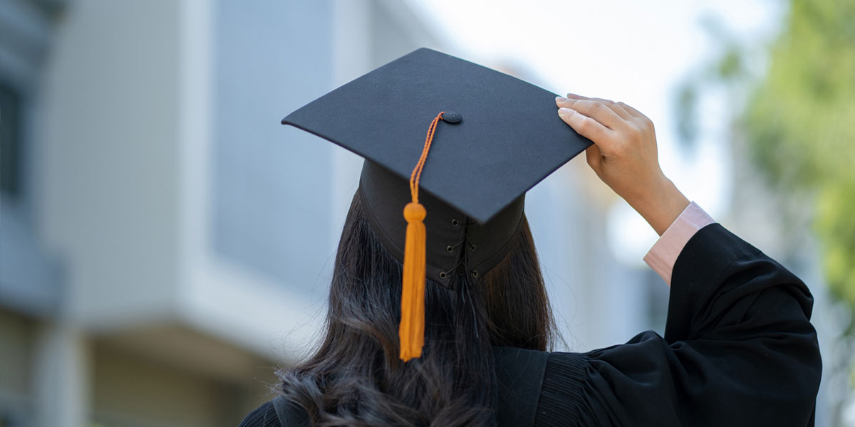College student with long black hair photographed from behind while wearing a graduation cap