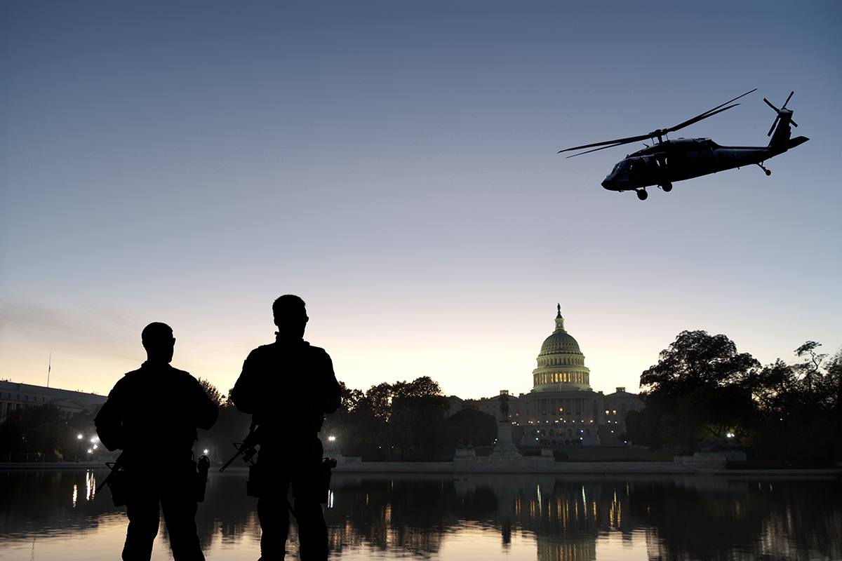 Silhouette of two armed guards and a helicopter in front of the US White House.