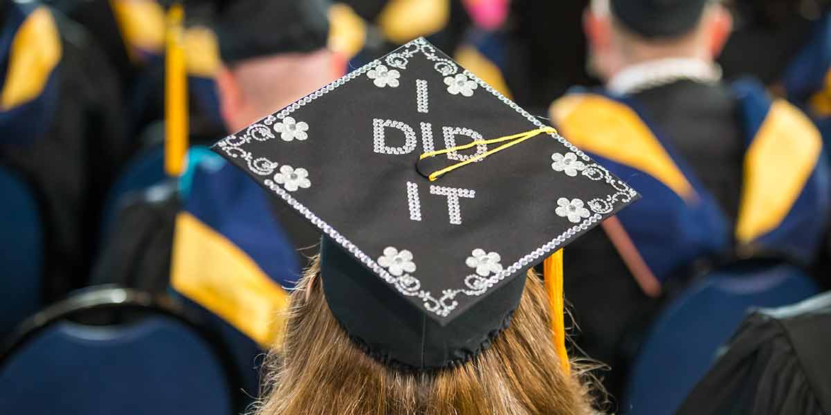 college student attending commencement and wearing a graduation cap decorated with the words "I did it"