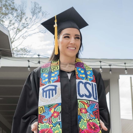 CSU graduate in her cap and gown with a colorful custom made drape